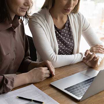 two women sitting in front of a laptop